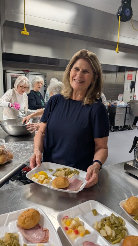 A First Christian Church of Allen volunteer holding a lunch plate while fellow volunteers prepare meals for seniors in Allen.